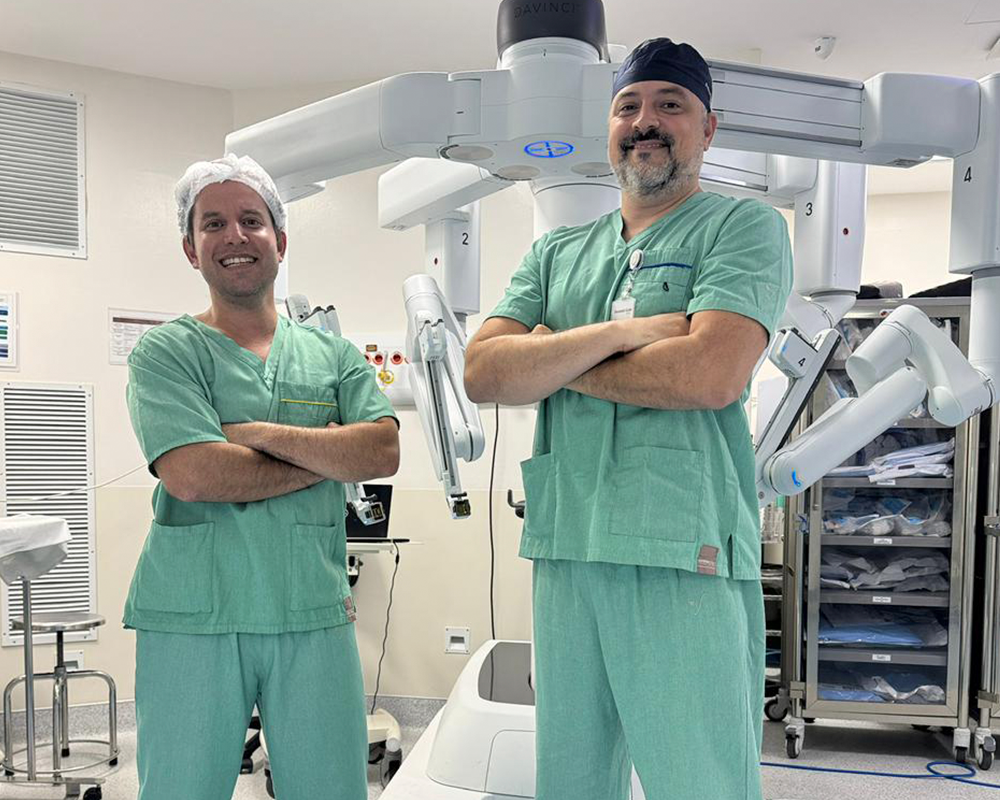 Dois cirurgiões com uniformes verdes e climatizadores no ambiente hospitalar.
