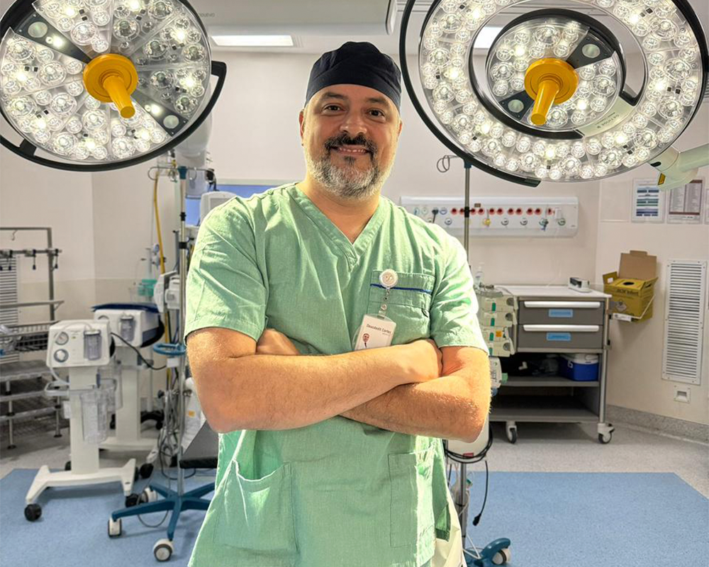 Profissional de saúde em sala de cirurgia com equipamentos médicos ao fundo.
